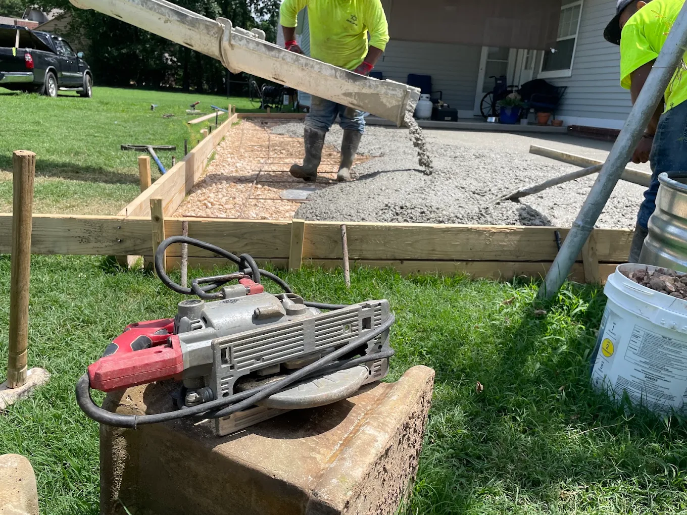 Crew pouring fresh concrete from a truck chute into wood forms for a walkway beside a house