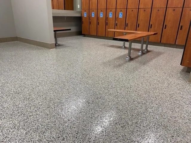 Gray and black flake epoxy floor in a locker room with wood lockers and benches