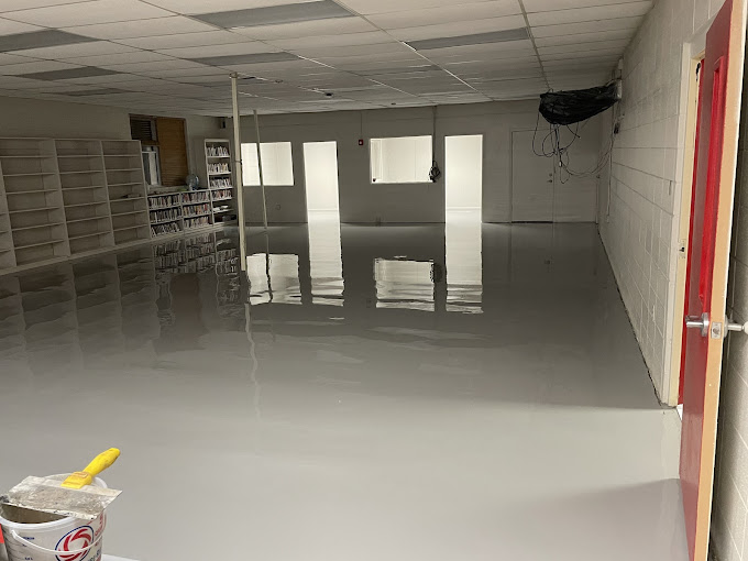 Freshly poured gray epoxy floor in a commercial interior with shelving along one wall