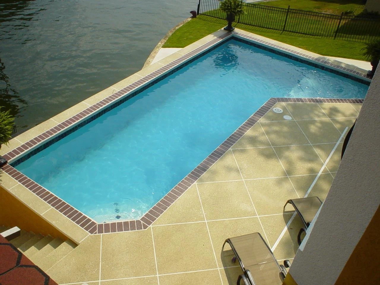 Resurfaced pool deck with a scored tile pattern and brick coping beside a lake