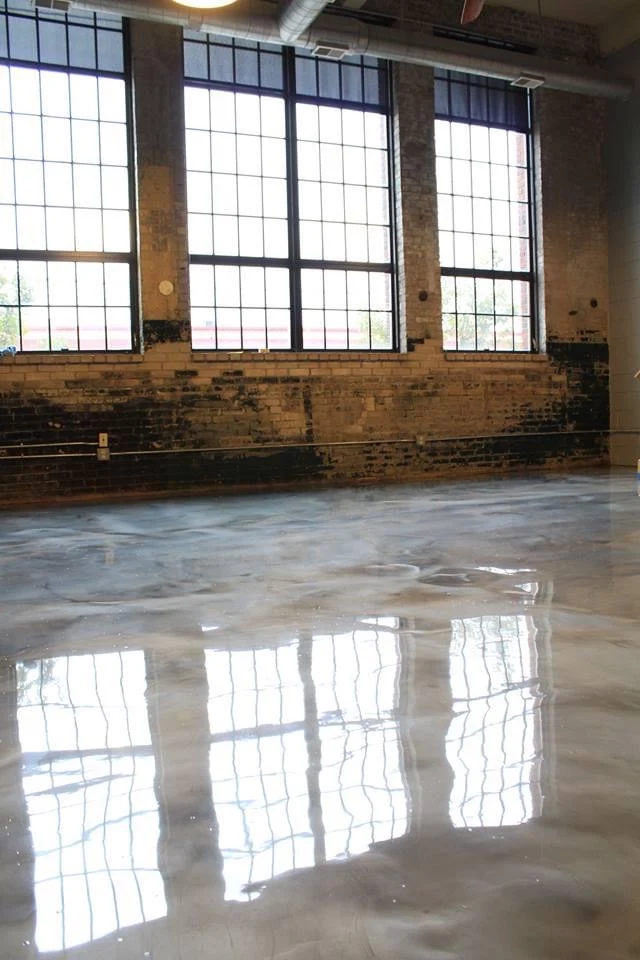 Glossy metallic epoxy floor reflecting tall factory windows in a renovated brick building
