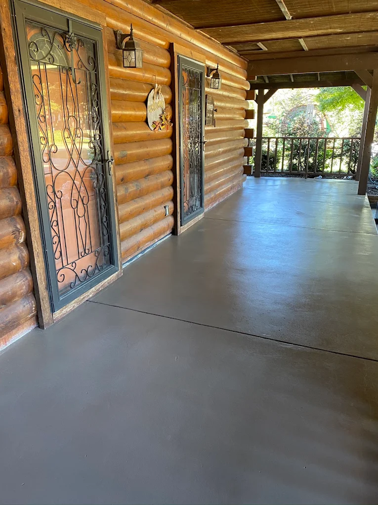 Coated gray concrete porch along a log home with iron-framed doors