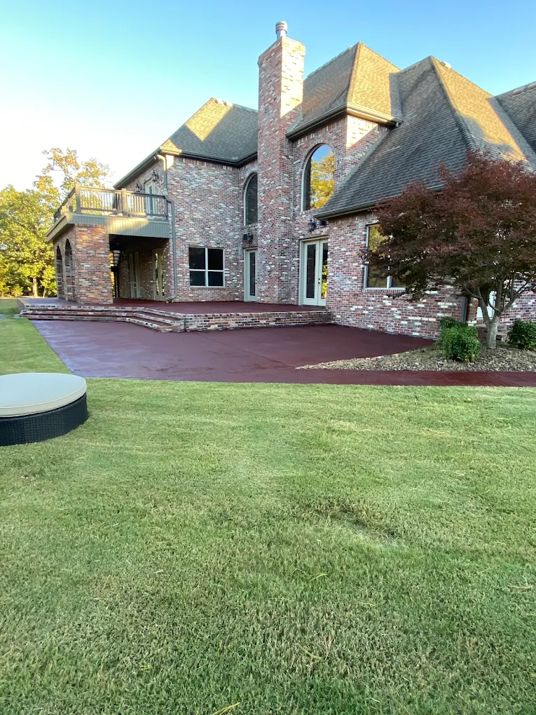 Red-stained concrete patio and steps behind a large brick home with a manicured lawn